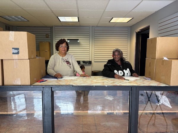Community in action: two team members behind the welcome counter with donation boxes in the program space