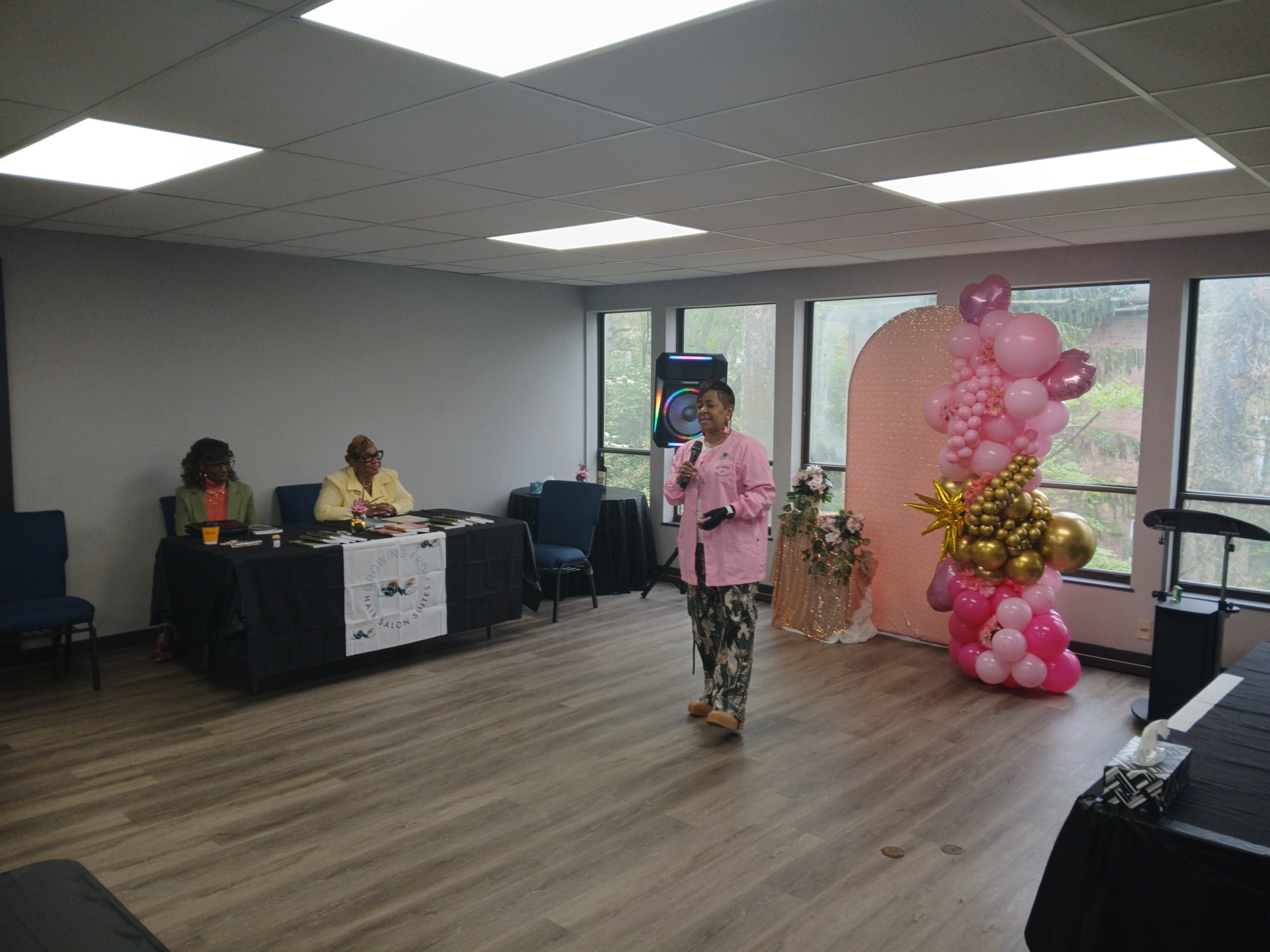 Panel at Growing From Love Hair Salon Suites: two speakers at a table with branded banner, balloons, and sequined backdrop