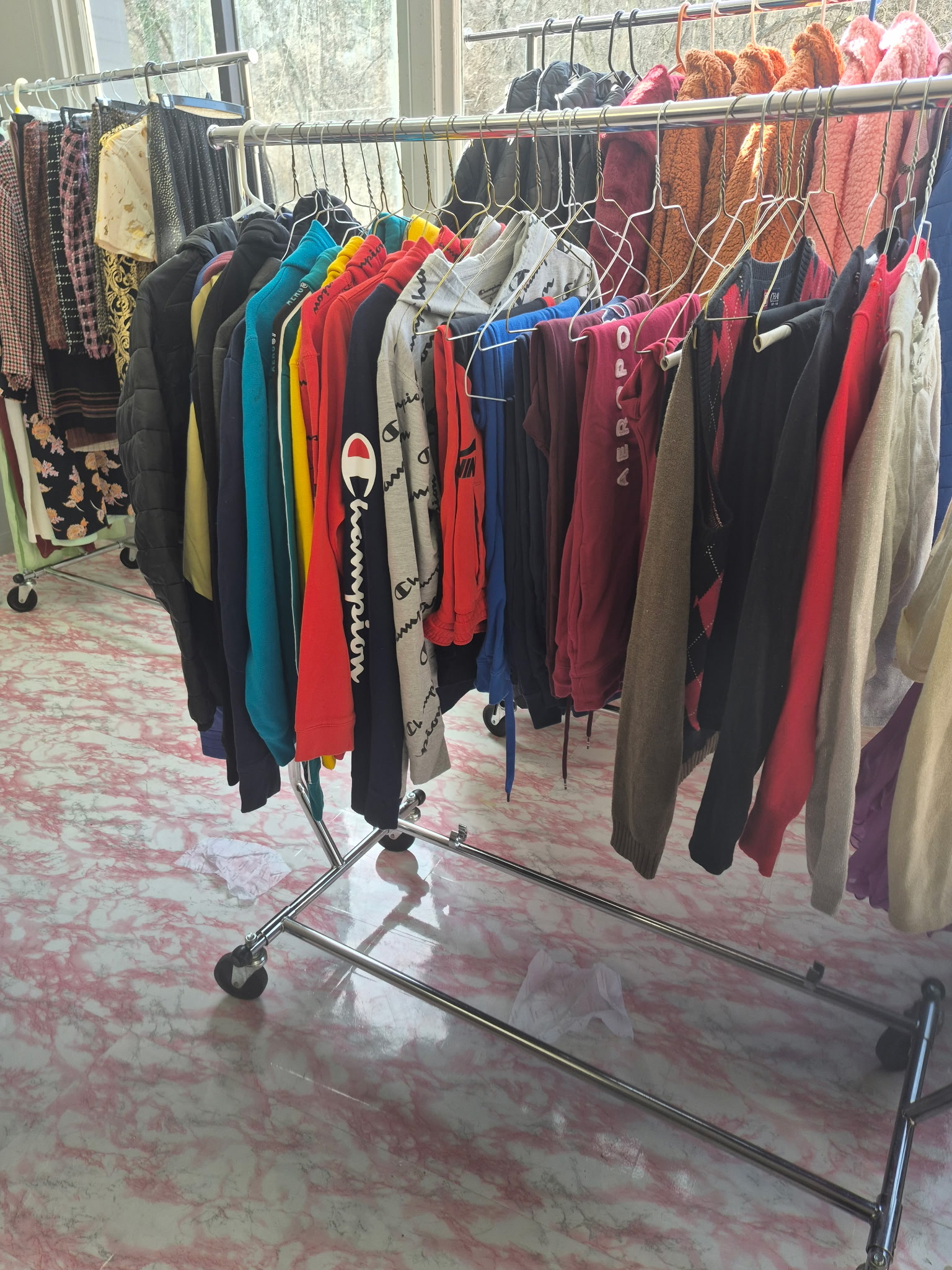 Rolling racks of hoodies, sweaters, and donated casual clothing by bright windows in the community closet