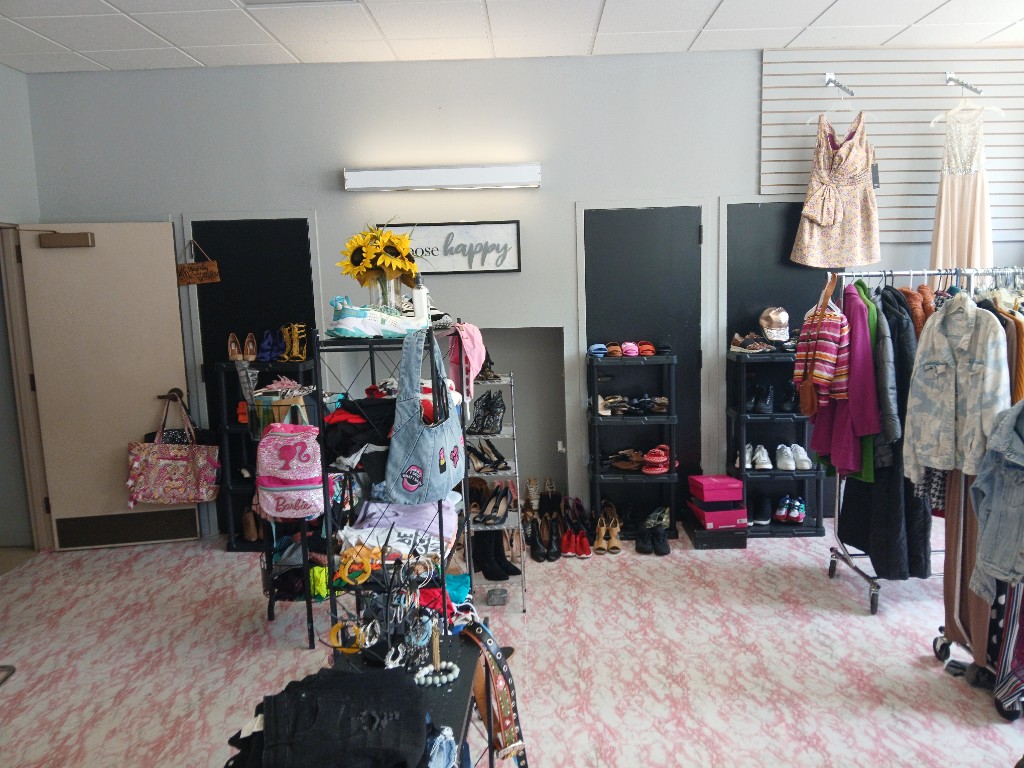 Community clothing closet: shoe displays, folded apparel on shelves, and hanging dresses by the choose happy sign