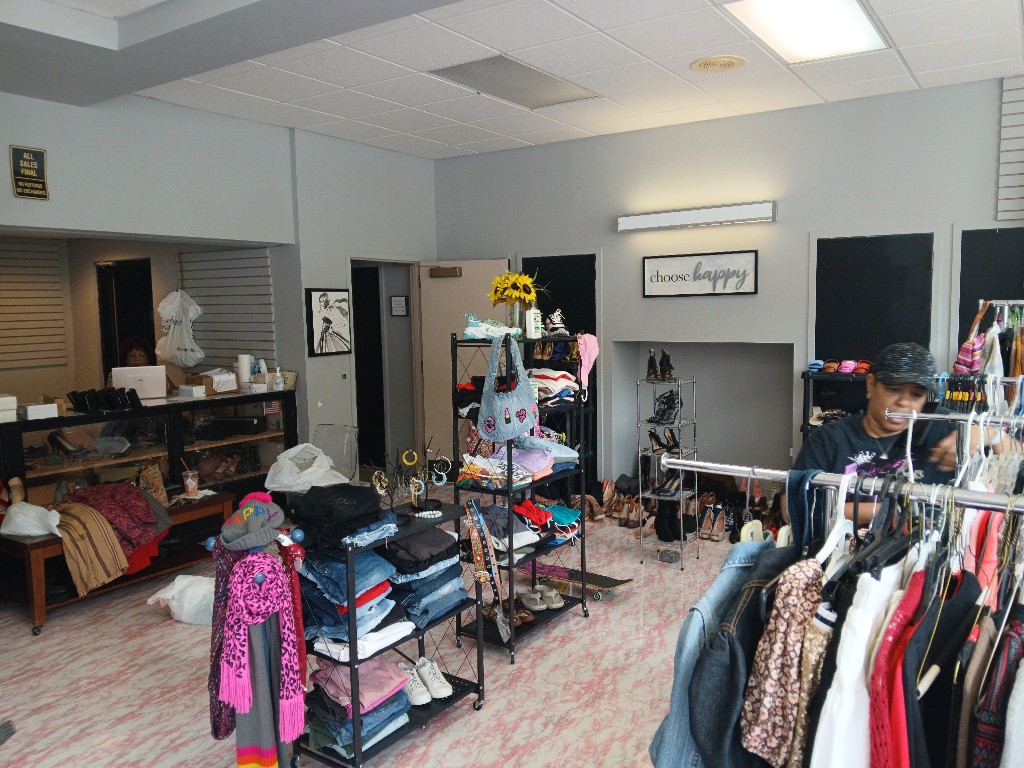 Community clothing closet: racks of hanging clothes, folded denim and sweaters on shelves, and sunflowers on a display unit